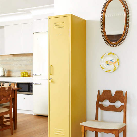 Yellow locker in a kitchen with wooden chairs and a mirror on the wall.