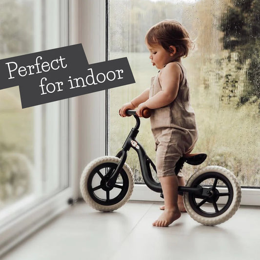 Child playing with a balance bike indoors near a window