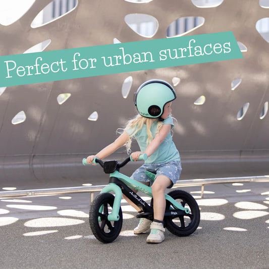 Child riding a green balance bike with a helmet, text 'Perfect for urban surfaces' above.