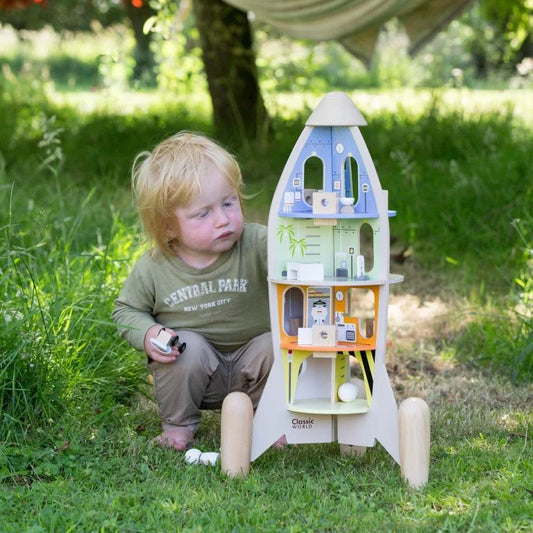 Child playing with a toy dollhouse in a grassy outdoor setting