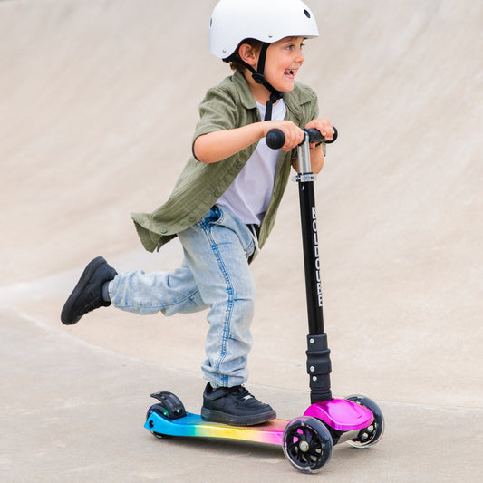 Child riding a scooter with colorful wheels on a plain background