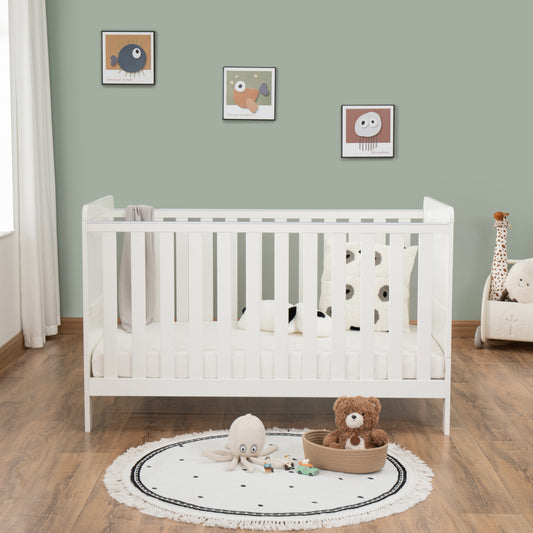 White cot  in a nursery with toys and decorative elements on a wooden floor.