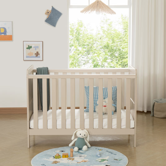 Baby cot in a bright room with toys and a rug on the floor.