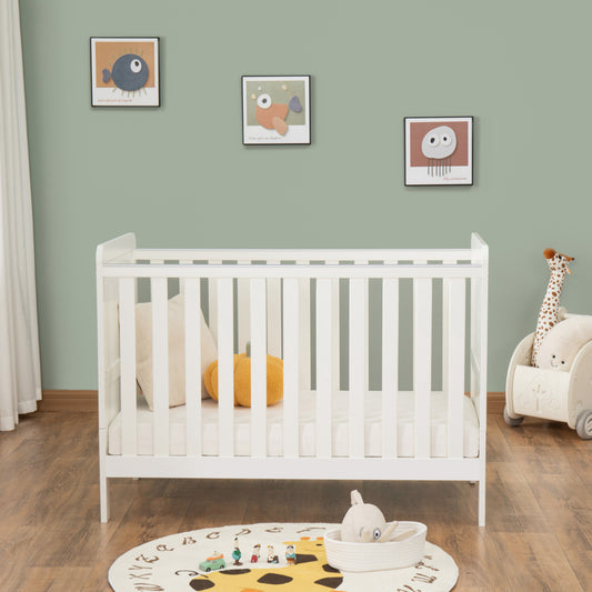 White cot in a nursery with toys and decorations on a green wall.