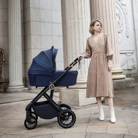 Woman in a beige dress standing next to a navy blue stroller in an architectural setting.