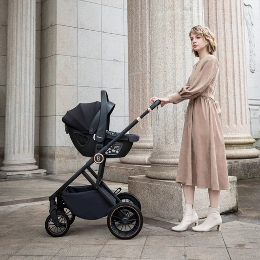 Woman in a beige dress pushing a black stroller in an urban setting with classical architecture.