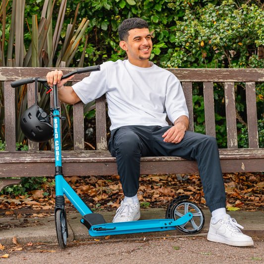 Man sitting on a bench with a blue scooter, wearing a helmet.