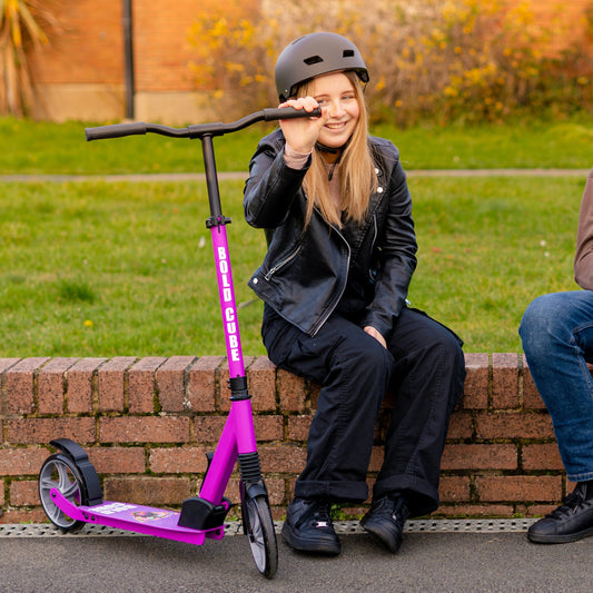 Person sitting on a brick wall with a pink scooter, wearing a helmet.