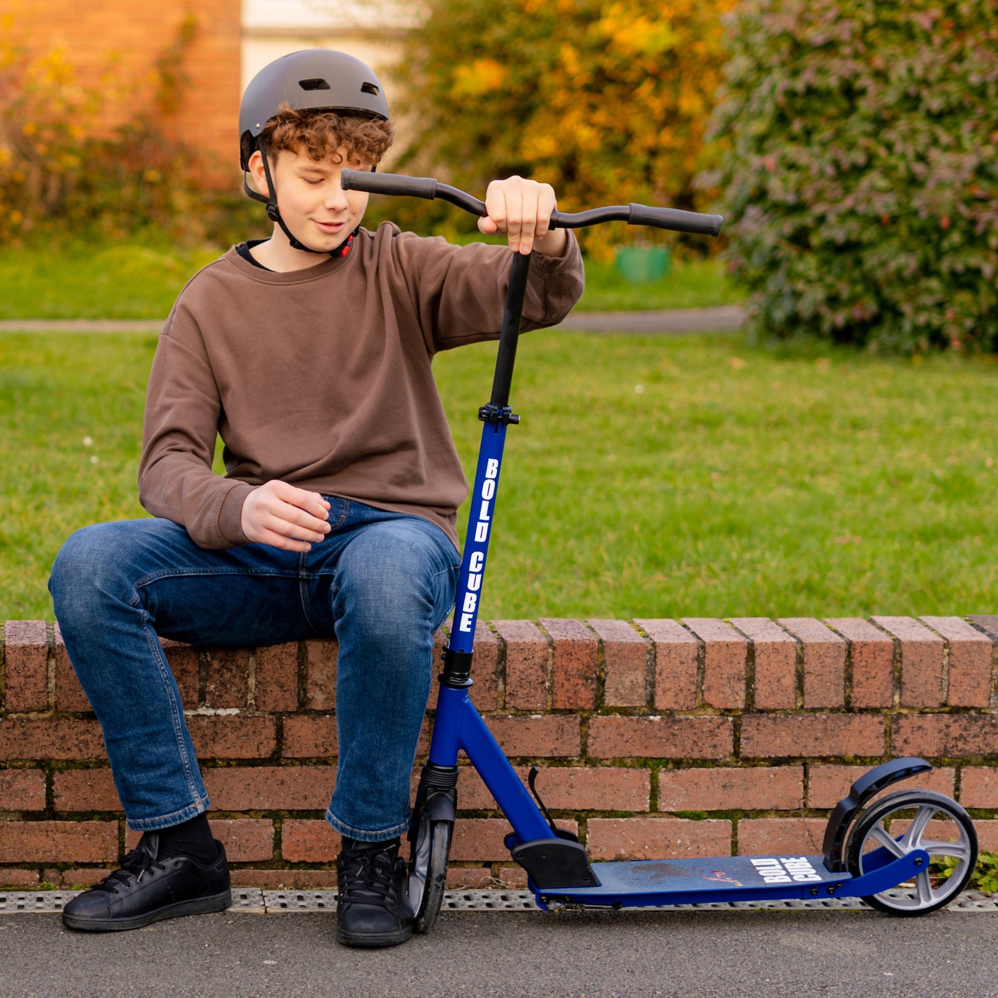 Child sitting on a brick wall with a blue scooter, wearing a helmet.
