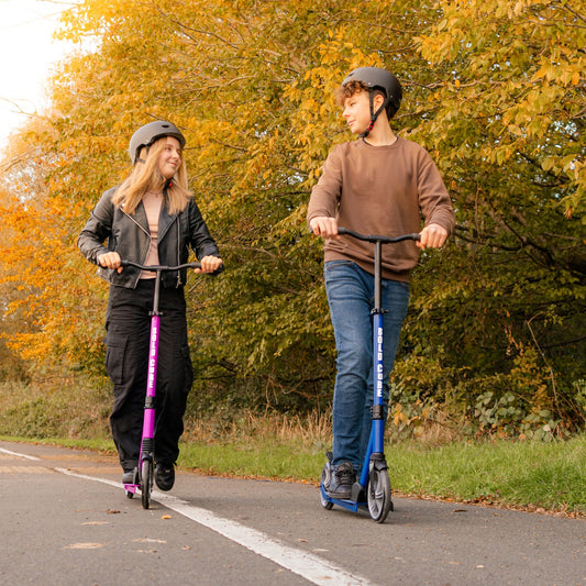 Two people riding scooters on a path with trees in the background