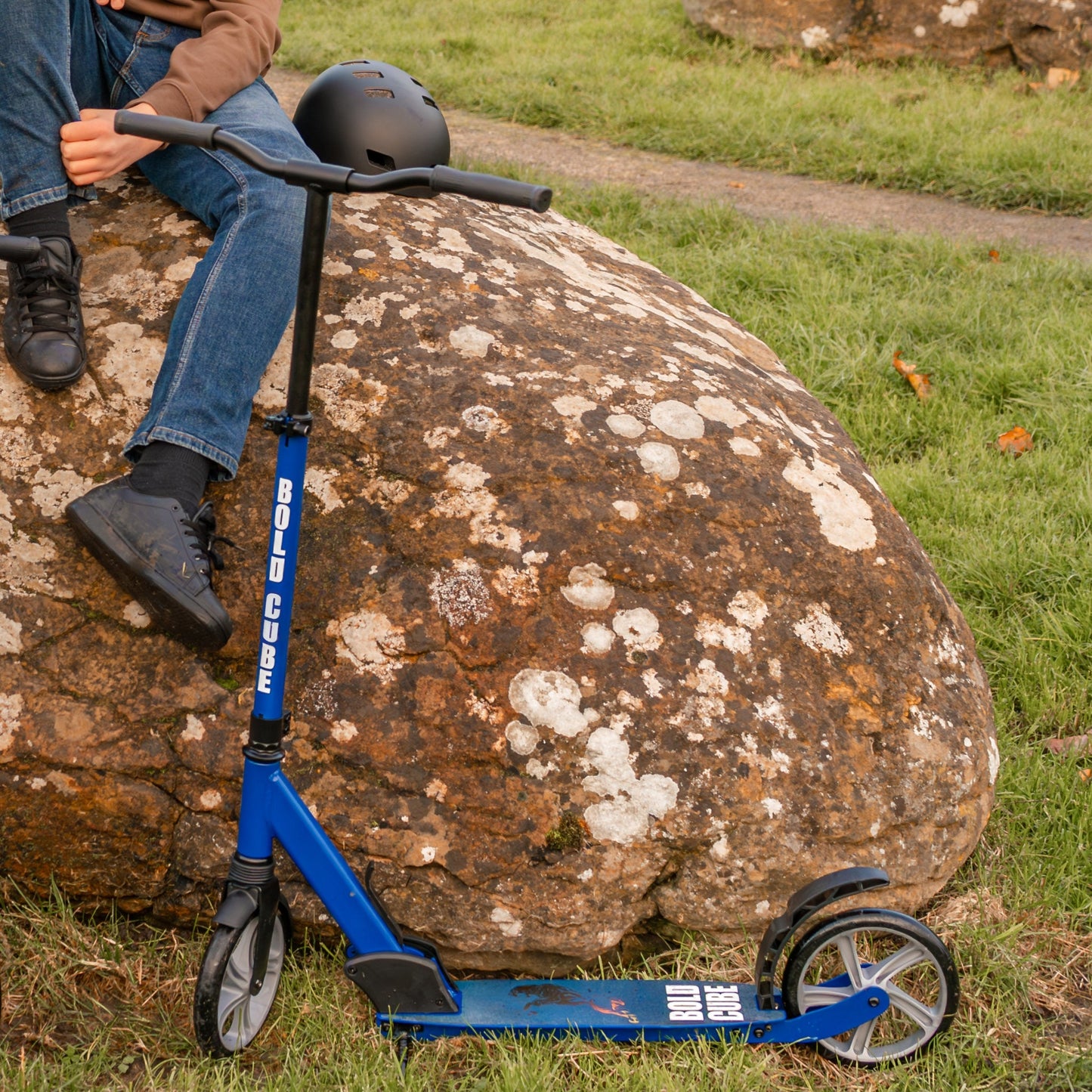 Person sitting on a rock with a blue scooter and helmet