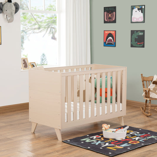 Nursery room with a cot, colourful rug, and toys on a wooden floor.