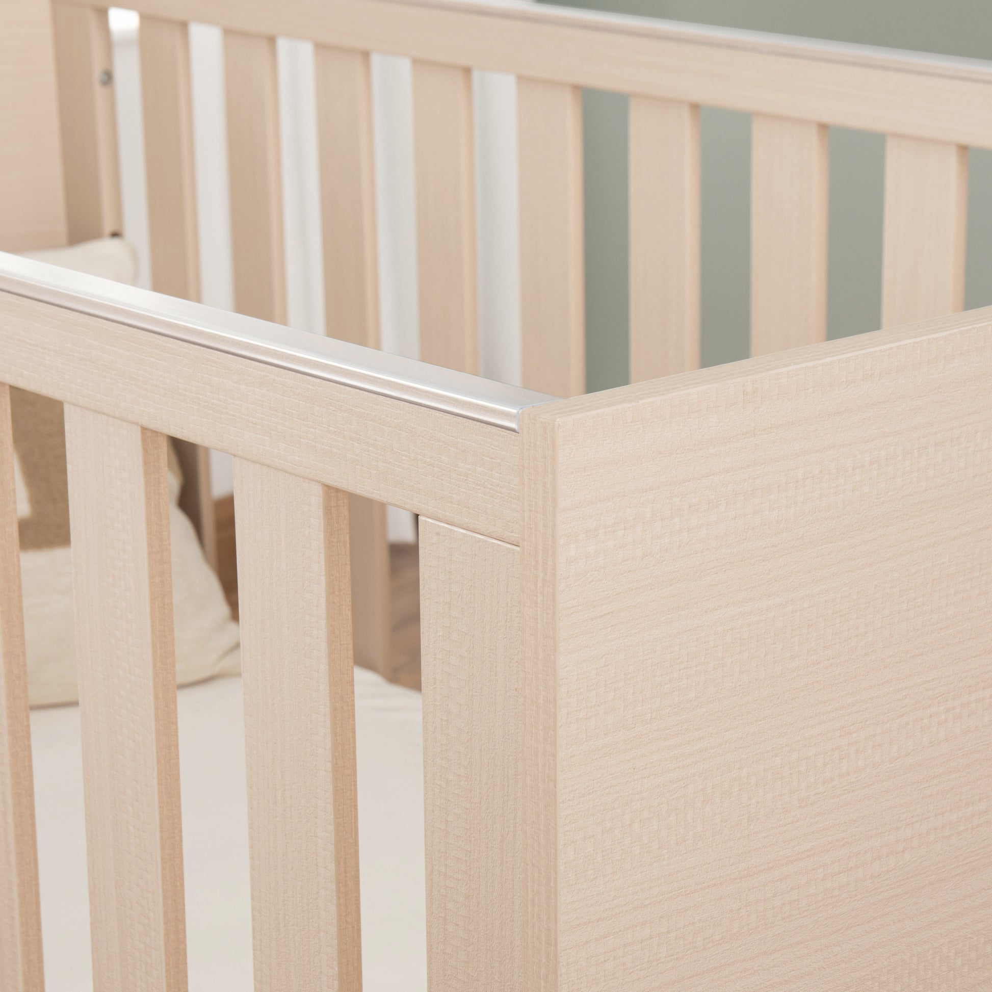Close-up of a wooden cot with teething rail with a neutral background