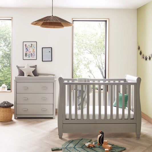 Nursery room with gray crib and dresser, large window, and decorative elements.