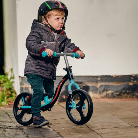 Child riding a balance bike with a helmet on a sidewalk.