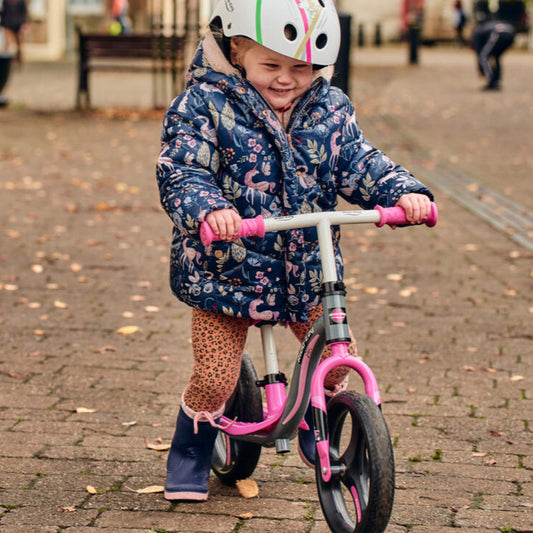 Child on a balance bike wearing a helmet and colorful coat in an outdoor setting