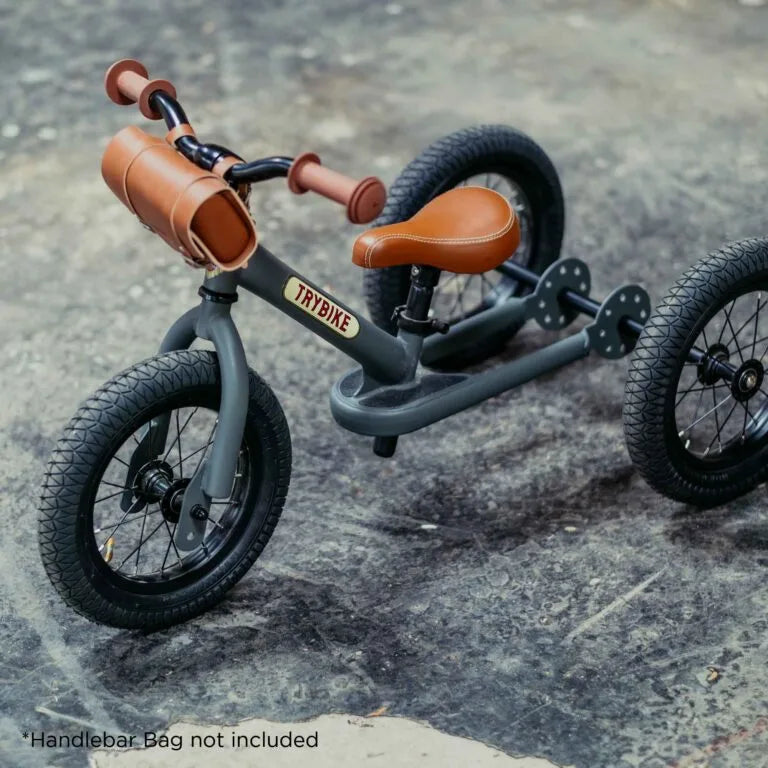 Children's balance bike with brown handlebar bag on a concrete surface