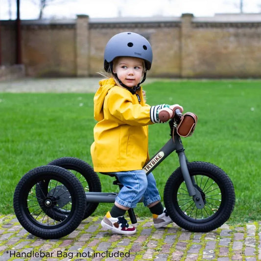Child riding a balance bike with training wheels on a paved path.