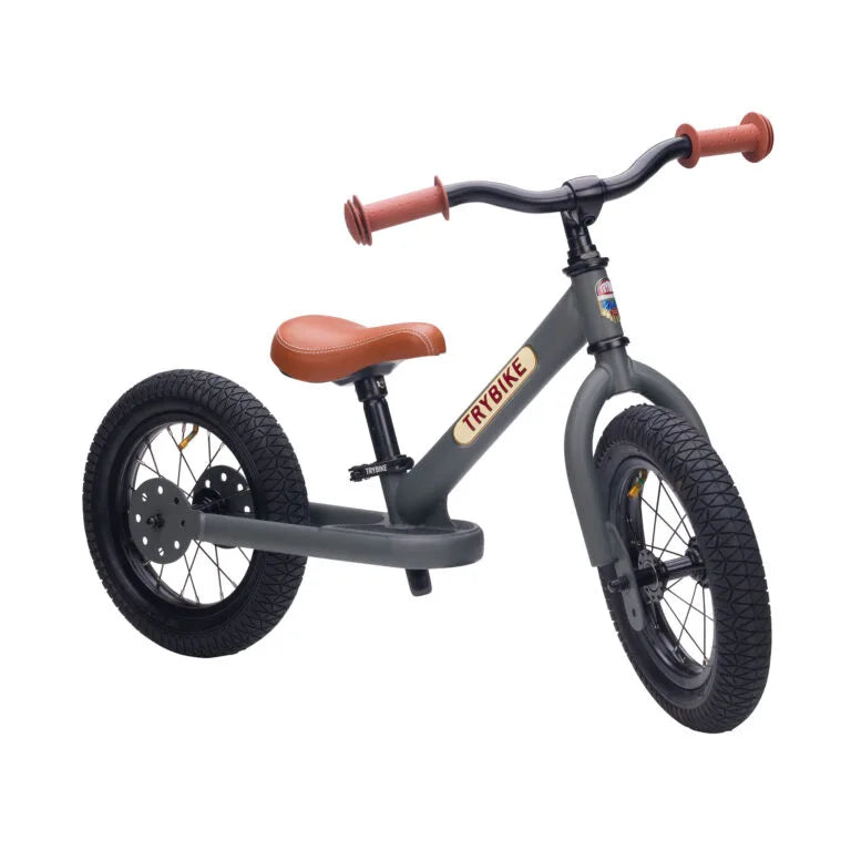 Children's balance bike with brown seat and handlebar grips on a white background