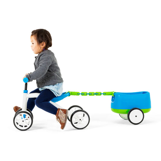 Child riding a balance bike with a blue and green trailer on a white background