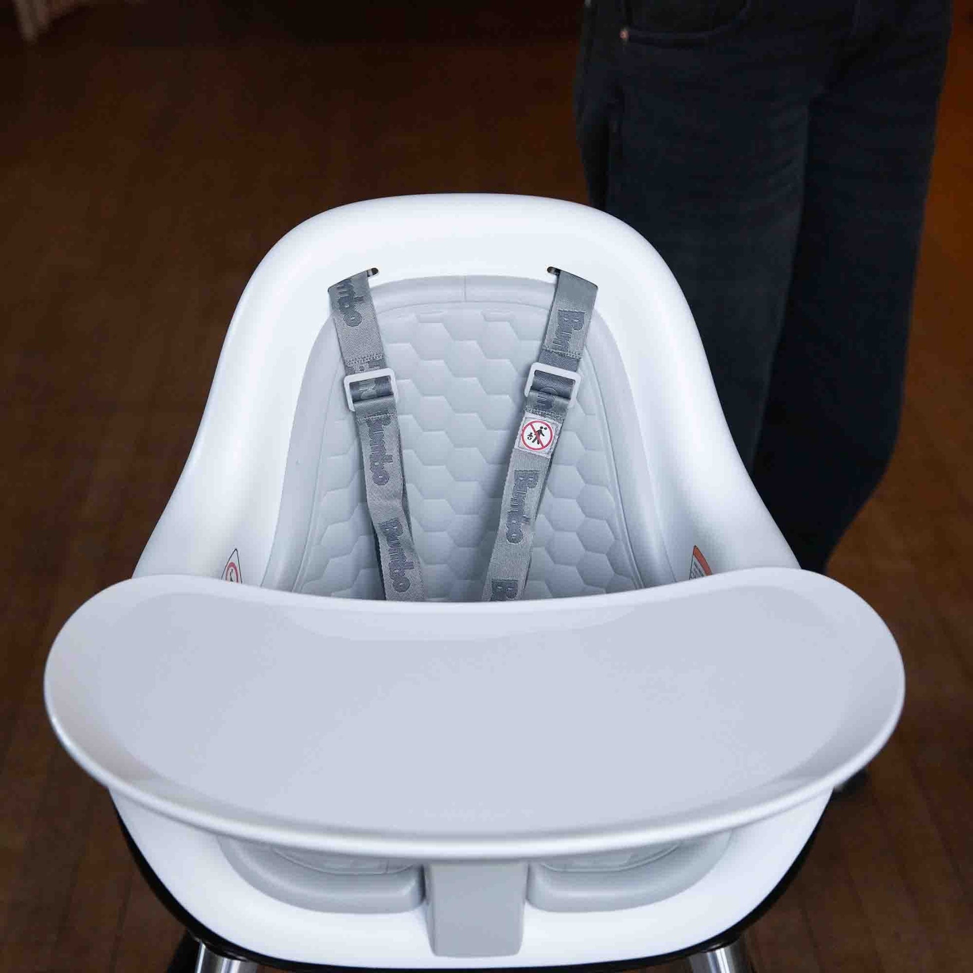White baby high chair with gray seat and straps on a wooden floor.
