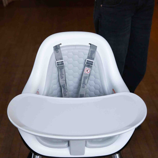 White baby high chair with gray seat and straps on a wooden floor.