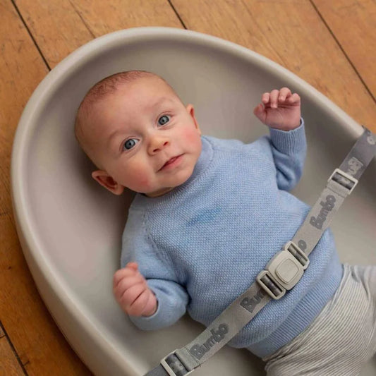 Baby in a blue sweater lying on a Boppy pillow with a wooden floor background
