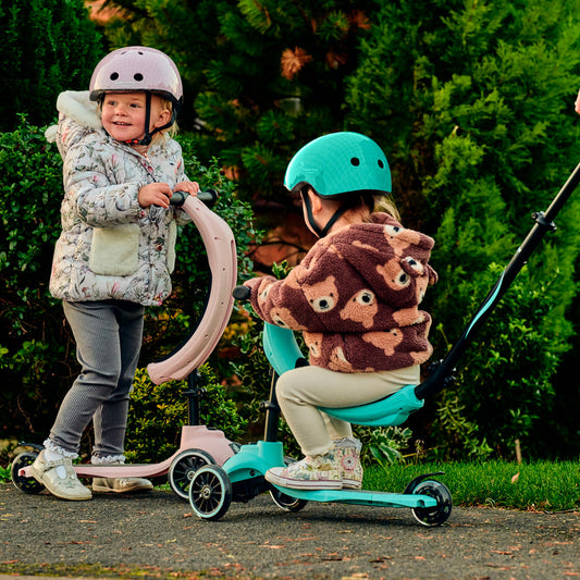 Two children on scooters with helmets in a park setting