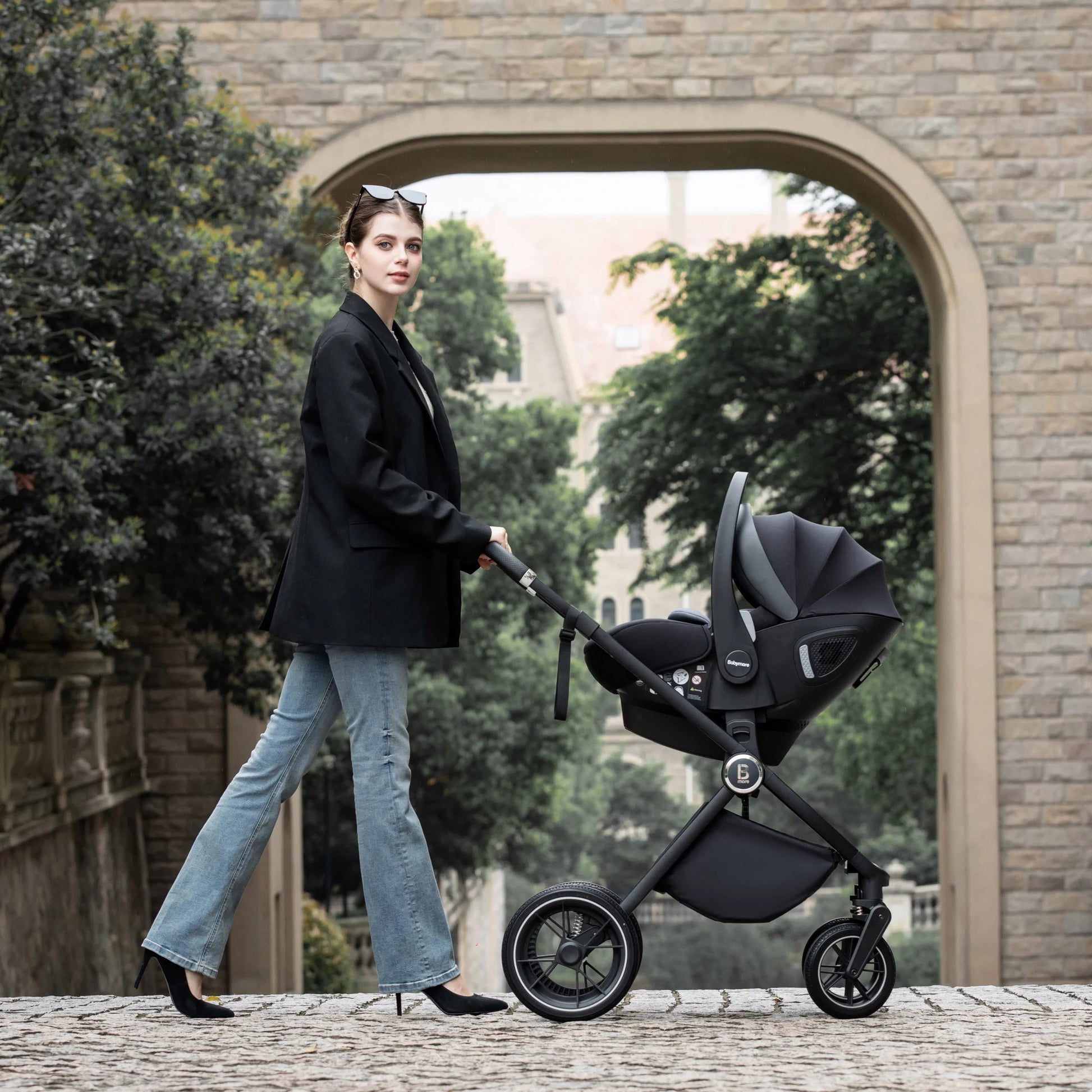 Woman pushing a black stroller in an outdoor setting with a stone archway and greenery.
