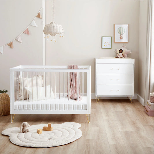 Nursery room with white crib and dresser on a wooden floor.