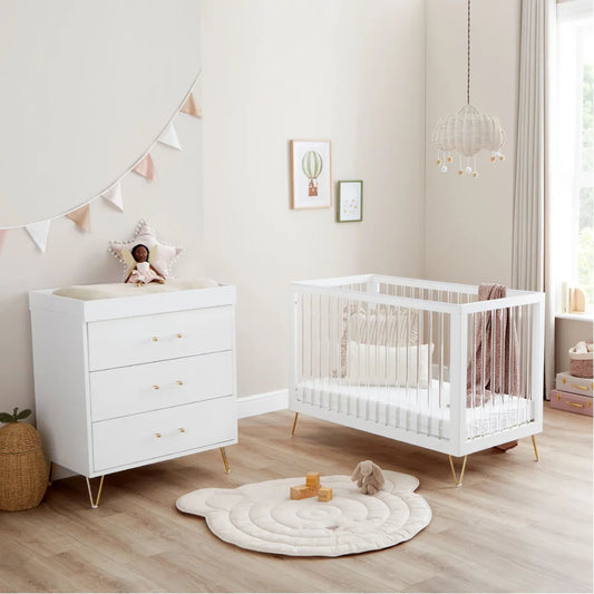 Nursery room with white crib and dresser on a wooden floor.