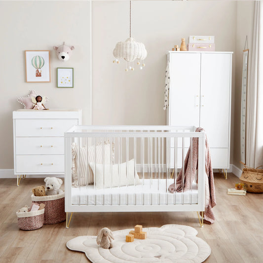 Nursery room with white crib, dresser, and toys on a wooden floor.