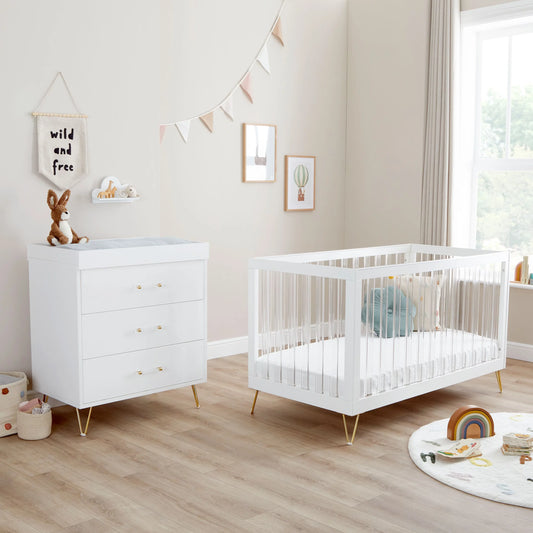 Nursery room with white crib and dresser in a bright room.