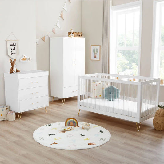 Nursery room with white crib, dresser, and round rug on wooden floor.