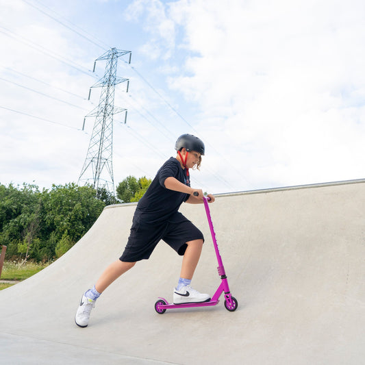 Person riding a pink scooter on a concrete ramp with a clear sky and power lines in the background