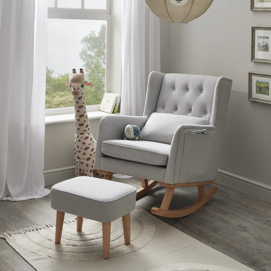 Gray rocking chair with ottoman and stuffed giraffe in a room with large windows.