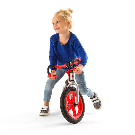 Child riding a balance bike with red wheels on a white background