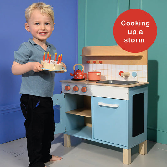 Child with a toy cake and play kitchen set against a blue and green background
