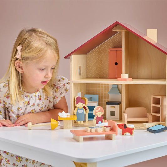 Child playing with a wooden dollhouse and accessories on a table.