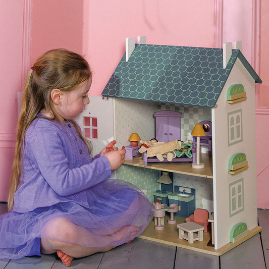 Young girl playing with a dollhouse in a room with pink walls.