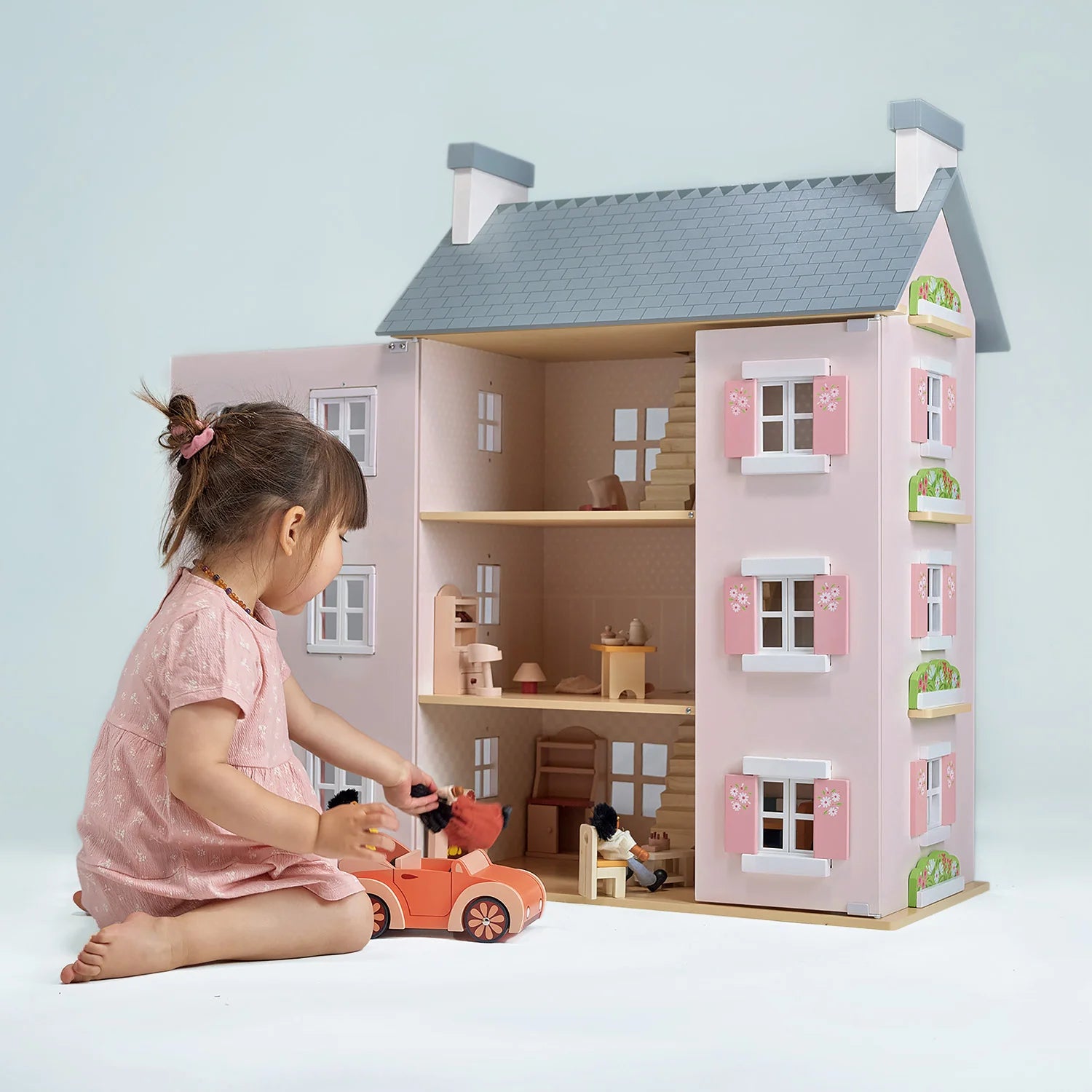 Child playing with a dollhouse and toy car on a light blue background