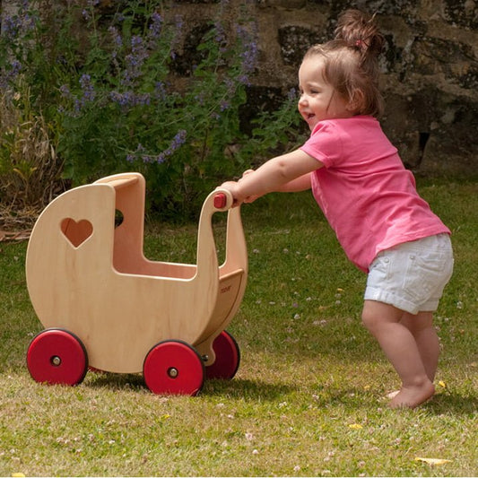 Child pushing a wooden doll pram outdoors on grass