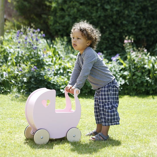 Child pushing a pink toy pram in a garden