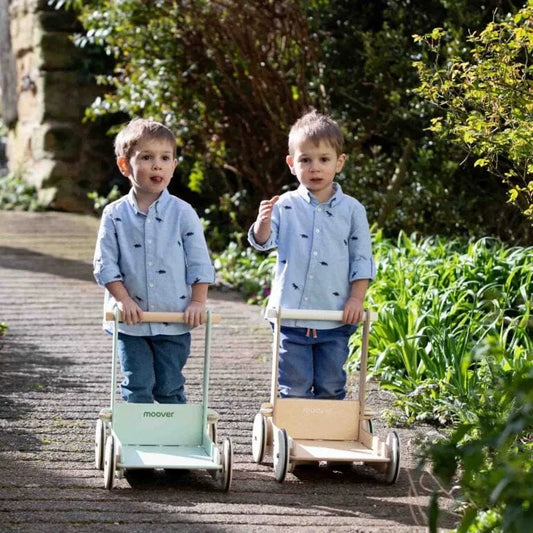 Two children pushing wooden toy carts in a garden setting