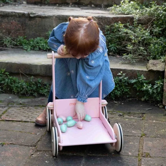 Child playing with a pink doll stroller outdoors