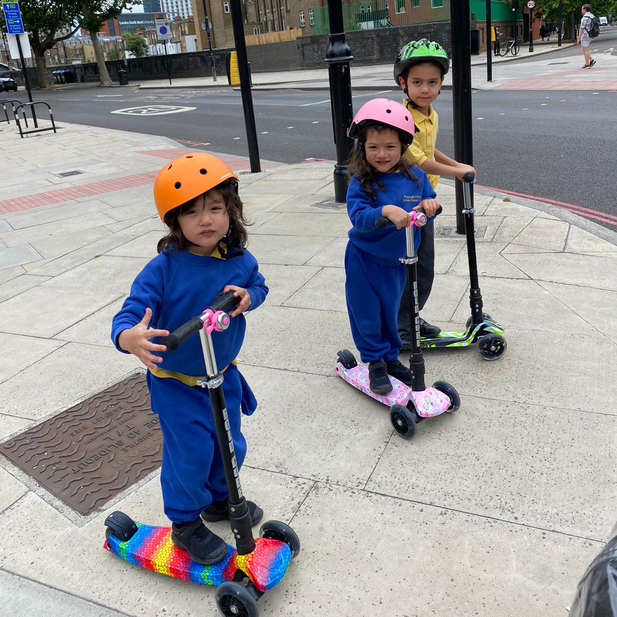 Children riding scooters on a sidewalk with helmets