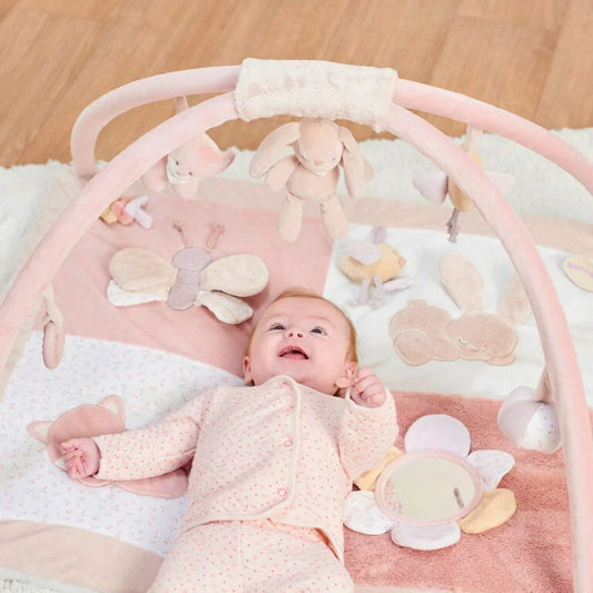 Baby lying on a pink play gym with various toys