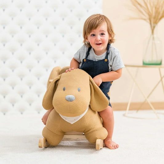 Child sitting on a plush dog-shaped toy in a room with a white textured wall and wooden floor.