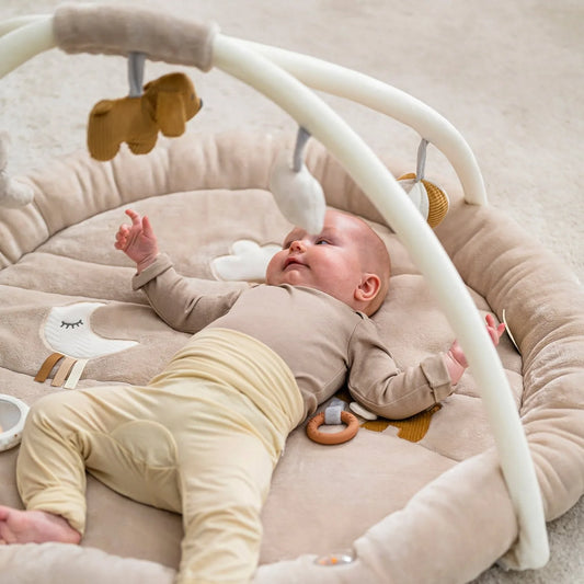 Baby lying on a soft surface with a baby bouncer and toys