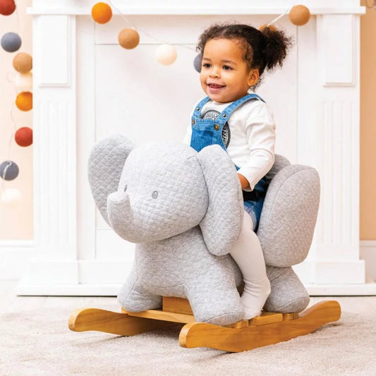 Child riding a gray elephant-shaped rocking toy in a room with colorful balloons.